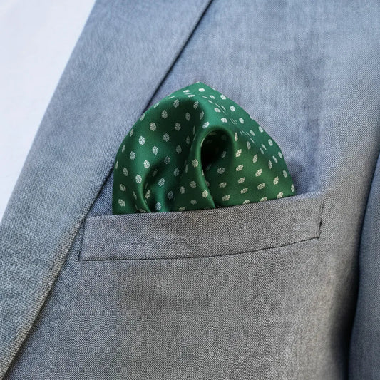 Green polka dot pocket square in a gray suit pocket against a light blue background